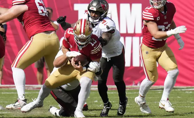 San Francisco 49ers quarterback Brock Purdy (13) is sacked by Tampa Bay Buccaneers defensive tackle Greg Gaines, bottom, as safety Jordan Whitehead (3) follows the play during the first half of an NFL football game in Tampa, Fla., Sunday, Nov. 10, 2024. (AP Photo/Chris O'Meara)