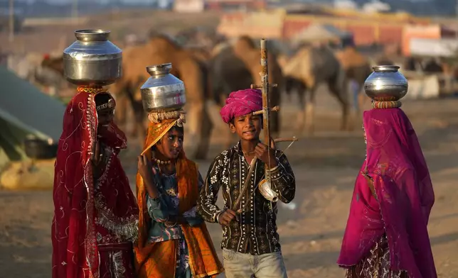 A child plays a string instrument as his companions carry water containers on their heads as they enact a scene from rural life during a camel fair in Pushkar, in the northwestern Indian state of Rajasthan, Wednesday, Nov. 13, 2024. (AP Photo/Deepak Sharma)