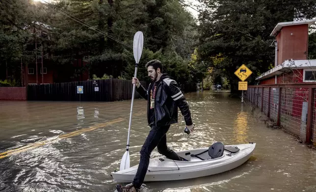 Tristan Millstone reacts as he steps in water after kayaking across a flooded section of Neely Road to buy groceries after a major storm in Guerneville, Calif., Saturday, Nov. 23, 2024. (Stephen Lam/San Francisco Chronicle via AP)