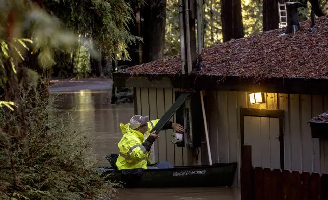 Sitting on a canoe, John Phillips works to shut down power at a flooded building at Mirabel RV Park &amp; Campground after a major storm in Forestville, Calif., Saturday, Nov. 23, 2024. (Stephen Lam/San Francisco Chronicle via AP)