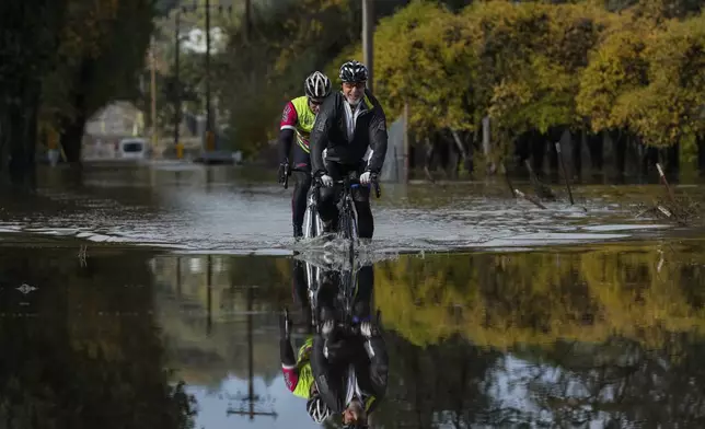 Dave Edmonds, right, and Mike Raasch ride their bicycles on a flooded road Saturday, Nov. 23, 2024, in Windsor, Calif. (AP Photo/Godofredo A. Vásquez)