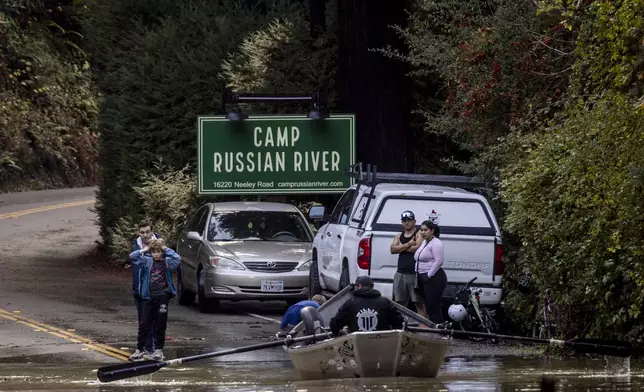 Residents watch as Ben Cote rows a boat across a flooded Neely road after a major storm in Guerneville, Calif., Saturday, Nov. 23, 2024. (Stephen Lam/San Francisco Chronicle via AP)