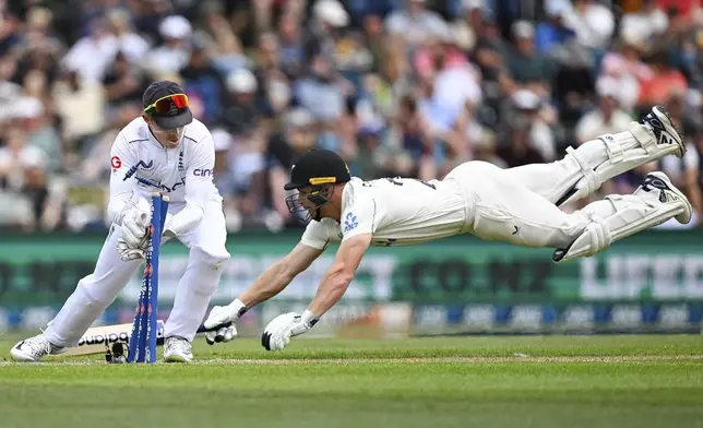 Glenn Phillips of New Zealand dives as England's wicketkeeper Ollie Pope knocks off the bails during play on the second day of the first cricket test between England and New Zealand at Hagley Oval in Christchurch, New Zealand, Friday, Nov. 29, 2024. (Andrew Cornaga/Photosport via AP)