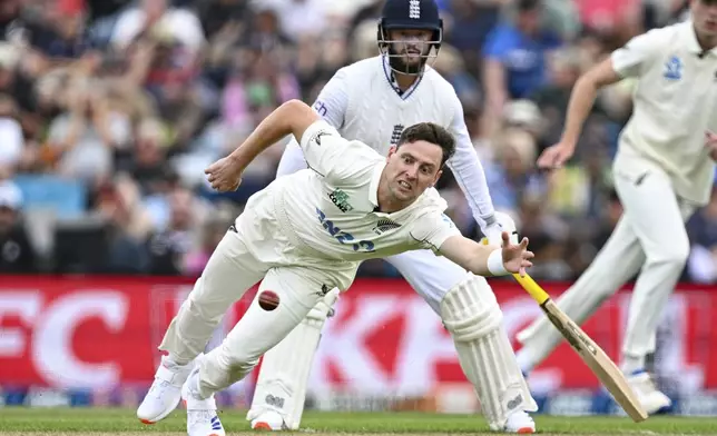 New Zealand's Matt Henry dives to field the ball as England's Ben Duckett watches during play on the second day of the first cricket test between England and New Zealand at Hagley Oval in Christchurch, New Zealand, Friday, Nov. 29, 2024. (Andrew Cornaga/Photosport via AP)