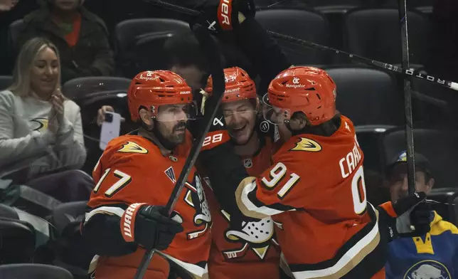 Anaheim Ducks defenseman Drew Helleson (43) celebrates after his goal with left wing Alex Killorn (17), and center Leo Carlsson (91) during the first period of an NHL hockey game against the Buffalo Sabres, Friday, Nov. 22, 2024, in Anaheim, Calif. (AP Photo/Kyusung Gong)