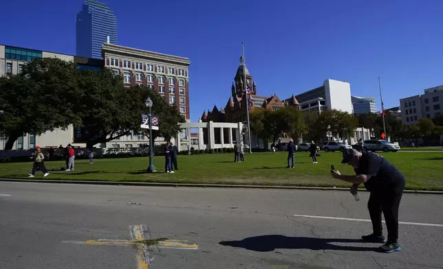 FILE - A person uses a cell phone to capture images of an X on Elm Street at Dealey Plaza, one of two spots marked where President John F. Kennedy was shot, as people gather on the 60th anniversary of his assassination, Nov. 22, 2023, in Dallas. (AP Photo/Julio Cortez, File)