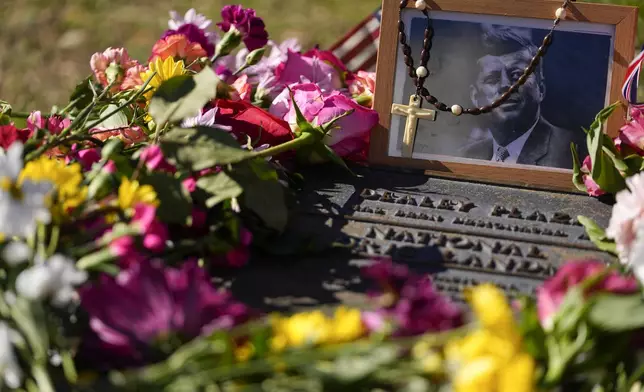 FILE - A rosary covers a photograph of President John F. Kennedy at a marker along Elm Street, where the former president was assassinated, as flowers adorn the memorial on the 60th anniversary of his assassination, Nov. 22, 2023, in Dallas. (AP Photo/Julio Cortez, File)