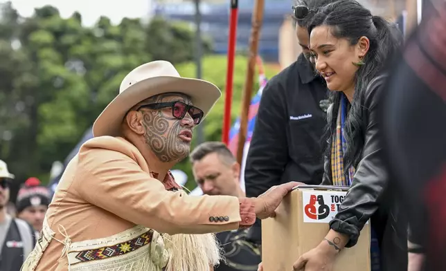 A petition is delivered to Member of Parliament Rawiri Waititi, left, outside New Zealand's parliament during a protest against a proposed law that would redefine the country's founding agreement between Indigenous Māori and the British Crown, in Wellington Tuesday, Nov. 19, 2024. (AP Photo/Mark Tantrum)