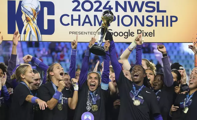 Orlando Pride forwards Marta, center, and Barbra Banda, right, lift the NWSL championship trophy together after defeating the Washington Spirit in an NWSL soccer game, Saturday, Nov. 23, 2024, in Kansas City, Mo. (AP Photo/Reed Hoffmann)