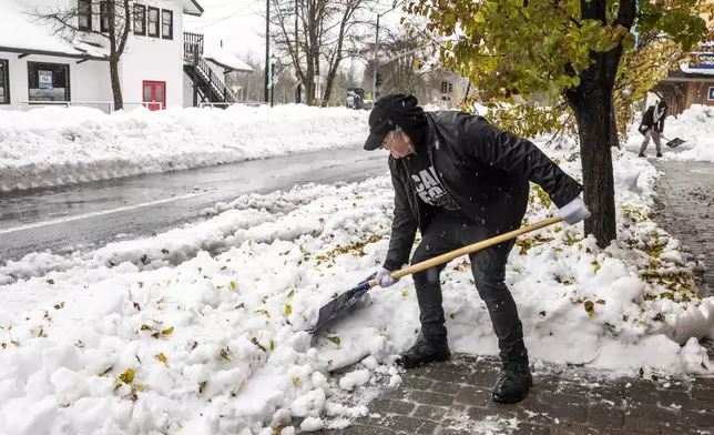 Salvador Garza shovels snow from the front of his shop Crystal Tones in Mt. Shasta, Calif.,, Thursday, Nov. 21, 2024, where runoff from rain and melting snow has begun to create standing water after an atmospheric river storm dumped significant precipitation in the area since Tuesday evening. (Carlos Avila Gonzalez/San Francisco Chronicle via AP)