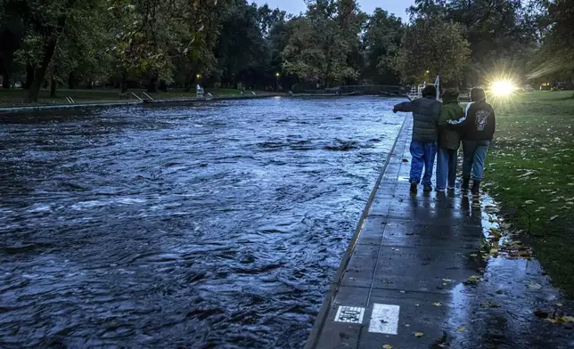 The Baer family, Larry, from left, Tiffany and their daughter Chloe stop to see Big Chico Creek swirling by a swimming area at One Mile Recreation Area, as runoff from Tuesday's rain and melting snow created flooding concerns from an atmospheric river storm that dumped significant precipitation in Chico, Calif., Thursday, Nov. 21, 2024. (Carlos Avila Gonzalez/San Francisco Chronicle via AP)