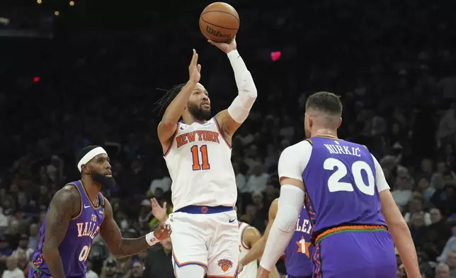 New York Knicks guard Jalen Brunson (11) gets off a shot between Phoenix Suns center Jusuf Nurkic (20) and forward Royce O'Neale, left, during the first half of an NBA basketball game Wednesday, Nov. 20, 2024, in Phoenix. (AP Photo/Ross D. Franklin)