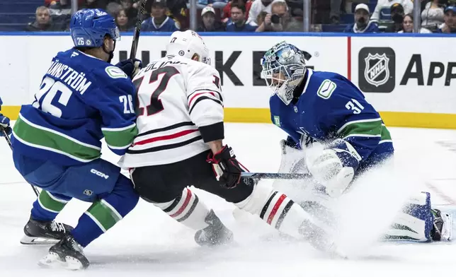 Vancouver Canucks goaltender Arturs Silovs (31) stops Chicago Blackhawks' Nick Foligno (17) as Vancouver's Erik Brannstrom (26) defends during the first period of an NHL hockey game in Vancouver, British Columbia, Saturday, Nov. 16, 2024. (Ethan Cairns/The Canadian Press via AP)