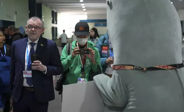 Dion George, South Africa environment minister, left, walks past a person in a dugong costume during the COP29 U.N. Climate Summit, Friday, Nov. 22, 2024, in Baku, Azerbaijan. (AP Photo/Peter Dejong)