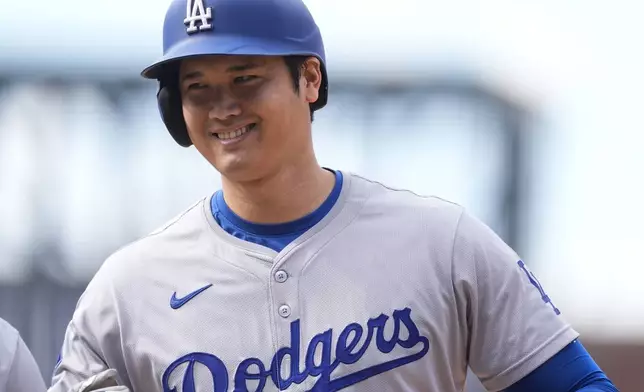 FILE - Los Angeles Dodgers' Shohei Ohtani smiles after reaching first base on a single off Colorado Rockies relief pitcher Seth Halvorsen in the eighth inning of a baseball game Sept. 29, 2024, in Denver. (AP Photo/David Zalubowski, File)