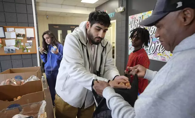 Volunteer Charles Mena, of Providence, R.I. center, places food in a bag for customer Hungria Hernandez Diomedes, right, in a food pantry at Federal Hill House, Tuesday, Nov. 12, 2024, in Providence, R.I. (AP Photo/Steven Senne)