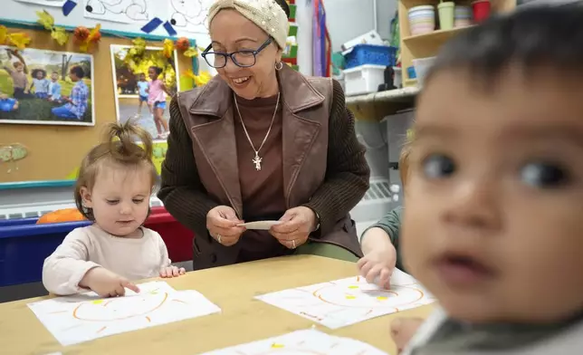 Volunteer Victoria Vasquez, 70, of Providence, R.I., center, supervises one-and-a-half year olds Scarlett Thomas, left, and Liam Echevarria Gaytan, right, in an early childcare program at Federal Hill House, Tuesday, Nov. 12, 2024, in Providence, R.I. (AP Photo/Steven Senne)