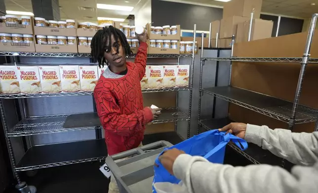 Volunteer Jaylund Asare, of Providence, R.I., center, assists Hungria Hernandez Diomedes, hands only at right, in a food pantry at Federal Hill House, Tuesday, Nov. 12, 2024, in Providence, R.I. (AP Photo/Steven Senne)