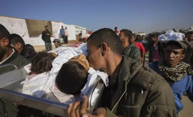 A man kisses the body one of three children as they are carried for burial in Khan Younis, Gaza Strip, Thursday Nov. 21, 2024. Seven-year-old Hamza, his five-year-old brother Abdelaziz, and his four-year-old sister Laila Hassan were among 9 people killed by an Israeli strike in Khan Younis on Wednesday. Palestinian health officials say the death toll in the Gaza Strip from the 13-month-old war between Israel and Hamas has surpassed 44,000. (AP Photo/Abdel Kareem Hana)