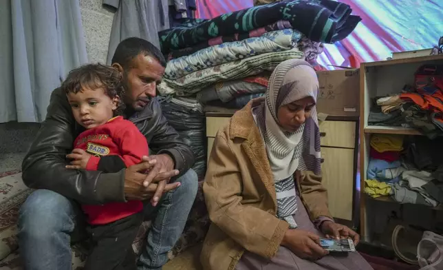 Areej al Qadi, right, shows a picture of one of her three dead children as her husband Mahmoud bin Hassan, left, holds a fourth surviving child at their tent in a refugee camp in Khan Younis, Gaza Strip, Thursday Nov. 21, 2024. Seven-year-old Hamza, his five-year-old brother Abdelaziz, and his four-year-old sister Laila Hassan were among 9 people killed by an Israeli strike in Khan Younis on Wednesday. Palestinian health officials say the death toll in the Gaza Strip from the 13-month-old war between Israel and Hamas has surpassed 44,000. (AP Photo/Abdel Kareem Hana)