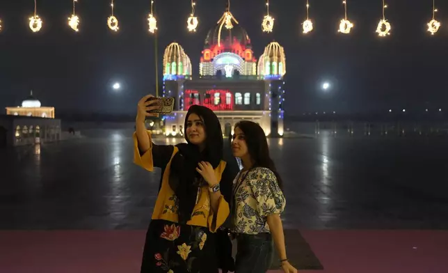 Sikh pilgrims take a selfie in front of the shrine of first Sikh guru, Guru Nanak Dev, which is illuminated for the birth anniversary celebrations at the Gurdwara Darbar Sahib in Kartarpur, Pakistan, Monday, Nov. 18, 2024. (AP Photo/Anjum Naveed)