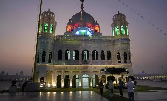 Sikh pilgrims arrive at the shrine of first Sikh guru, Guru Nanak Dev, which is illuminated for the birth anniversary celebrations at the Gurdwara Darbar Sahib in Kartarpur, Pakistan, Monday, Nov. 18, 2024. (AP Photo/Anjum Naveed)