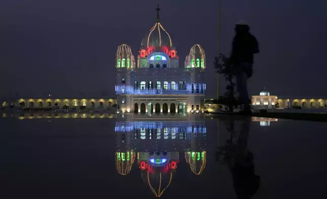 A photographer positions himself to take photos at the shrine of first Sikh guru, Guru Nanak Dev, which is illuminated for the birth anniversary celebrations at the Gurdwara Darbar Sahib in Kartarpur, Pakistan, Monday, Nov. 18, 2024. (AP Photo/Anjum Naveed)