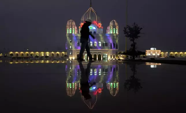 A photographer positions himself to take photos at the shrine of first Sikh guru, Guru Nanak Dev, which is illuminated for the birth anniversary celebrations at the Gurdwara Darbar Sahib in Kartarpur, Pakistan, Monday, Nov. 18, 2024. (AP Photo/Anjum Naveed)