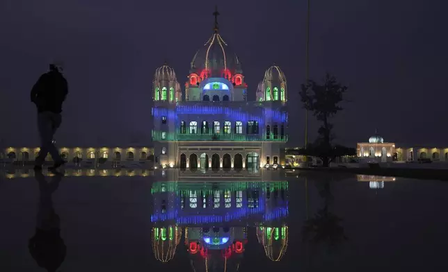 A photographer positions himself to take photos at the shrine of first Sikh guru, Guru Nanak Dev, which is illuminated for the birth anniversary celebrations at the Gurdwara Darbar Sahib in Kartarpur, Pakistan, Monday, Nov. 18, 2024. (AP Photo/Anjum Naveed)