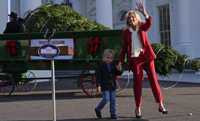 First lady Jill Biden waves as she walks with her grandson Beau Biden after receiving the official 2024 White House Christmas Tree on the North Portico of the White House in Washington, Monday, Nov. 25, 2024. Cartner's Christmas Tree Farm from Newland, N.C., provided the Fraser fir that will be displayed in the Blue Room of the White House. (AP Photo/Susan Walsh)