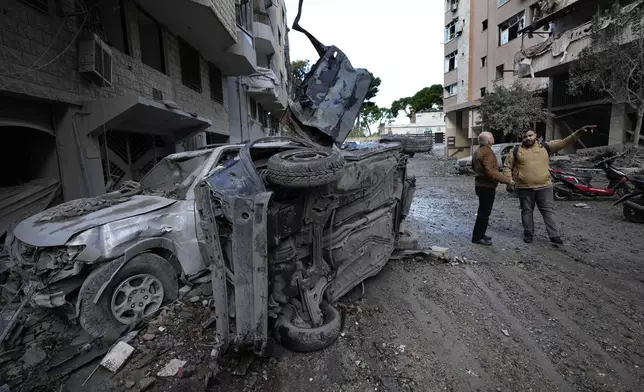 Residents stand near to cars that were destroyed after Sunday's Israeli airstrike in Dahiyeh, in the southern suburb of Beirut, Lebanon, Monday, Nov. 25, 2024. (AP Photo/Hussein Malla)