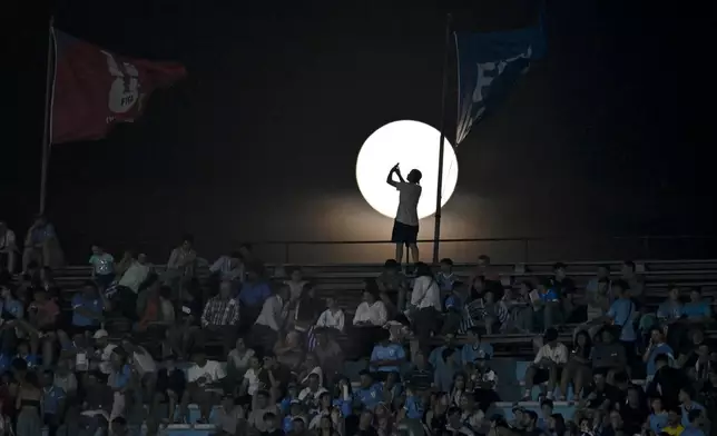 A fan takes a picture of the moon prior to a qualifying soccer match for the FIFA World Cup 2026 between Uruguay and Colombia in Montevideo, Uruguay, Friday, Nov. 15, 2024. (AP Photo/Santiago Mazzarovich)