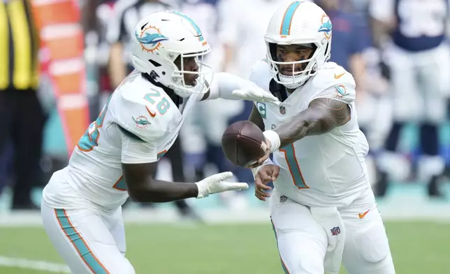 Miami Dolphins quarterback Tua Tagovailoa (1) hands the ball to running back De'Von Achane (28) during the first half of an NFL football game against the New England Patriots, Sunday, Nov. 24, 2024, in Miami Gardens, Fla. (AP Photo/Wilfredo Lee)