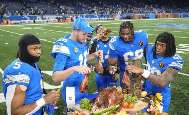 Detroit Lions running back David Montgomery (5) from left, quarterback Jared Goff (16), wide receiver Amon-Ra St. Brown (14), linebacker Al-Quadin Muhammad (69), and running back Jahmyr Gibbs (26) celebrate with turkey after beating the Chicago Bears 23-20 in an NFL football game in Detroit, Thursday, Nov. 28, 2024. (AP Photo/Carlos Osorio)