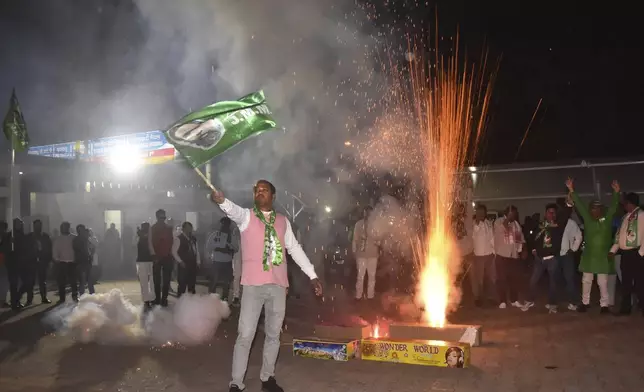 A supporter of Jharkhand Mukti Morcha waves party flag while others burn firecrackers as they celebrate their party's win in state assembly election in Ranchi, in the Indian state of Jharkhand, Saturday, Nov. 23, 2024. (AP Photo/Rajesh Kumar)