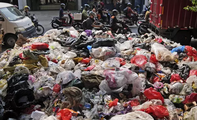 Motorists ride past garbage, most of them plastic, piled up on the side of a road in Jakarta, Indonesia, Tuesday, Nov. 26, 2024. (AP Photo/Dita Alangkara)