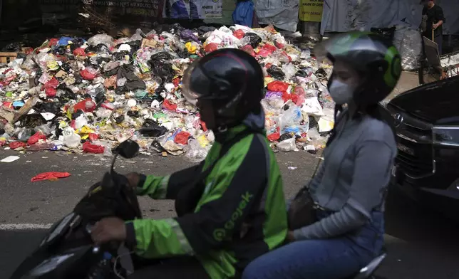 Motorists ride past garbage, most of them plastic, piled up on the side of a road in Jakarta, Indonesia, Tuesday, Nov. 26, 2024. (AP Photo/Dita Alangkara)