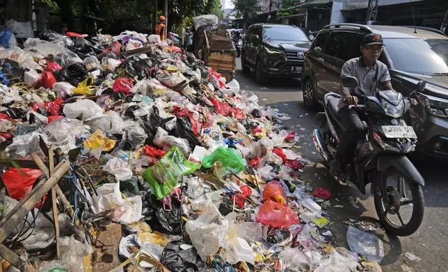 Motorists ride past garbage, most of them plastic, piled up on the side of a road in Jakarta, Indonesia, Tuesday, Nov. 26, 2024. (AP Photo/Dita Alangkara)