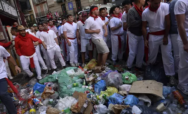 FILE- Revelers stand near a pile of garbage before a bullrun with bulls from La Palmosilla ranch during the first day of the running of the bulls at the San Fermín fiestas in Pamplona, Spain, Sunday, July 7, 2024. (AP Photo/Alvaro Barrientos, File)