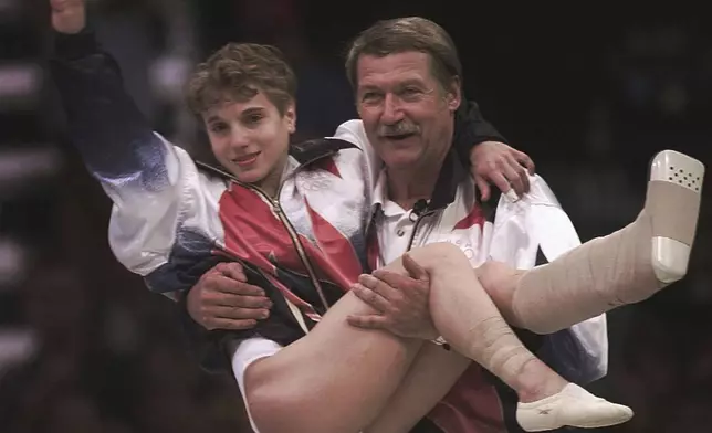 FILE - USA's Kerri Strug is carried by her coach, Bela Karolyi, as she waves to the crowd on her way to receiving her gold medal for the women's team gymnastics competition, at the Centennial Summer Olympic Games in Atlanta, July 23, 1996. Strug had two torn ligaments and a sprained ankle from the vault competition. (AP Photo/Susan Ragan, File)