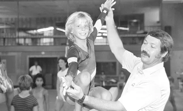 FILE - Olympic gymnastics coach Bela Karolyi, right, instructs Sara Tank on the balance beam at his Olympic training facility in north Houston, Aug. 12, 1985. (AP Photo/Richard J. Carson, File)