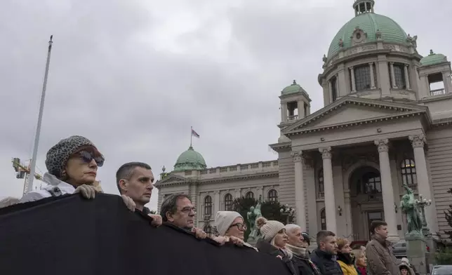 People hold a black banner and stand in silence in front of the Serbian parliament to commemorate the 15 victims of a railway station roof collapse in Belgrade, Serbia, Friday, Nov. 29, 2024. (AP Photo/Marko Drobnjakovic)