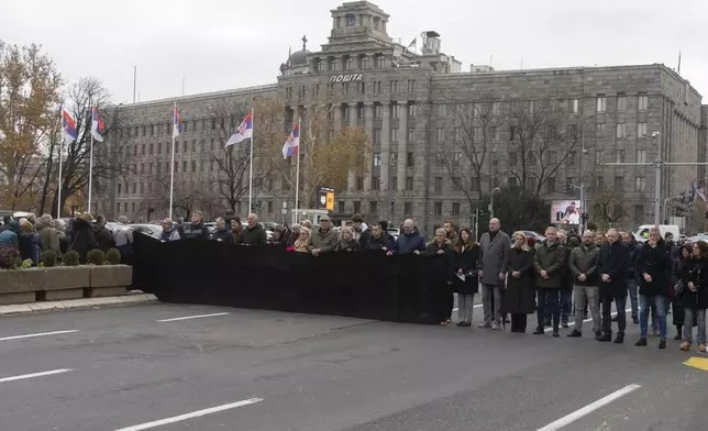 People hold a black banner and stand in silence to commemorate the 15 victims of a railway station roof collapse in Belgrade, Serbia, Friday, Nov. 29, 2024. (AP Photo/Marko Drobnjakovic)