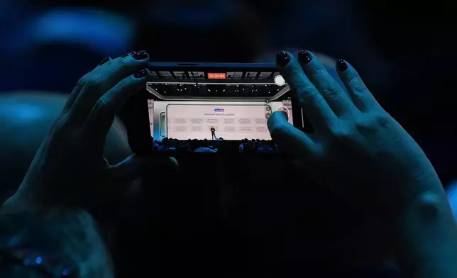 An attendee at the Microsoft Ignite conference records CEO Satya Nadella as he delivers the keynote address at the conference Tuesday, Nov. 19, 2024, in Chicago. (AP Photo/Charles Rex Arbogast)