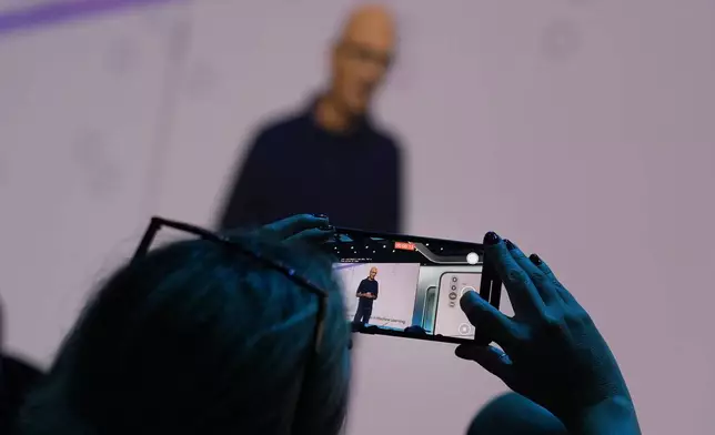 An attendee at the Microsoft Ignite conference records CEO Satya Nadella as he delivers the keynote address at the conference Tuesday, Nov. 19, 2024, in Chicago. (AP Photo/Charles Rex Arbogast)