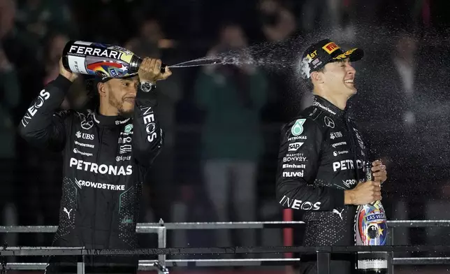 Mercedes driver Lewis Hamilton, of Britain, left, sprays champagne on race winner Mercedes driver George Russell, of Britain, after the F1 Las Vegas Grand Prix auto race, Saturday, Nov. 23, 2024, in Las Vegas. (AP Photo/Rick Scuteri)