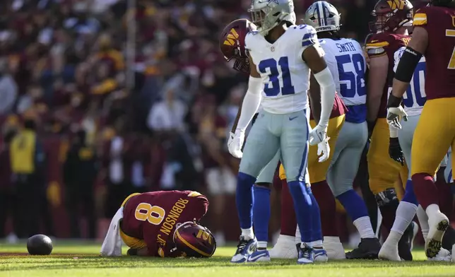 Washington Commanders running back Brian Robinson Jr. (8) lays on the ground after sustaining an injury during the first half of an NFL football game against the Dallas Cowboys, Sunday, Nov. 24, 2024, in Landover, Md. (AP Photo/Stephanie Scarbrough)