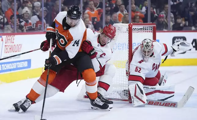 Philadelphia Flyers' Sean Couturier (14) tries to move puck against Carolina Hurricanes' Jordan Staal (11) and Pyotr Kochetkov (52) the during the second period of an NHL hockey game, Wednesday, Nov. 20, 2024, in Philadelphia. (AP Photo/Matt Slocum)