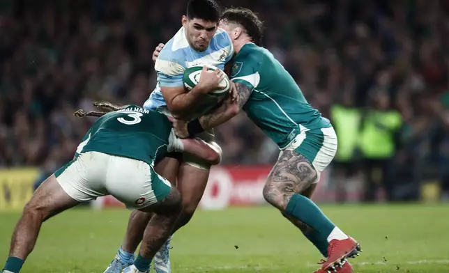 Argentina's Joaquin Oviedo, centre, is tackled by Ireland's Finlay Bealham, left, during the Autumn Nations series rugby union match between Ireland and Argentina, at Aviva Stadium, Dublin, Ireland, Friday, Nov. 15, 2024. (AP Photo/Peter Morrison)