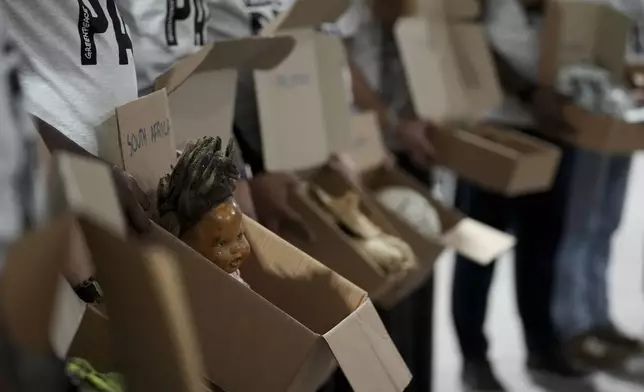 Demonstrators wearing shirts that say "make polluters pay" hold items that were recovered by support teams from extreme weather events and displayed at the COP29 U.N. Climate Summit, Monday, Nov. 18, 2024, in Baku, Azerbaijan. (AP Photo/Sergei Grits)